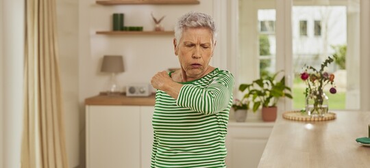 Eine Frau hustet in die Armbeuge, da der festsitzende Schleim ihre Gesundheit beeinträchtigt.