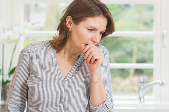 Frau mit verschleimten Bronchien hustet, welches eine Folge chronischer Atemwegserkrankungen sein kann
